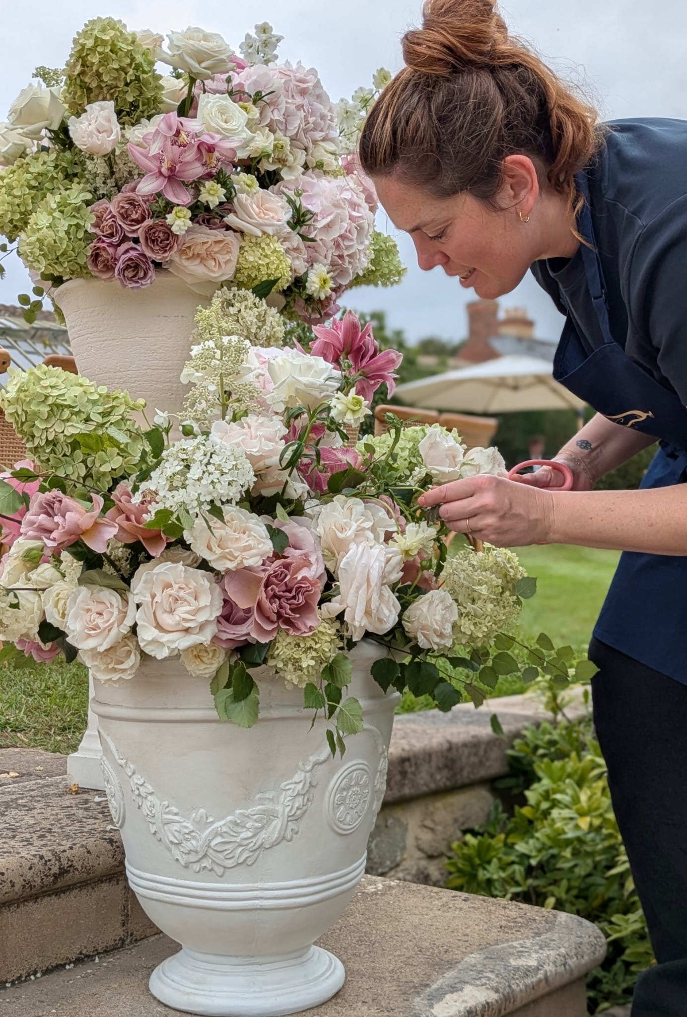Hayley arranging a large floral urn installation with roses, hydrangea and lilies