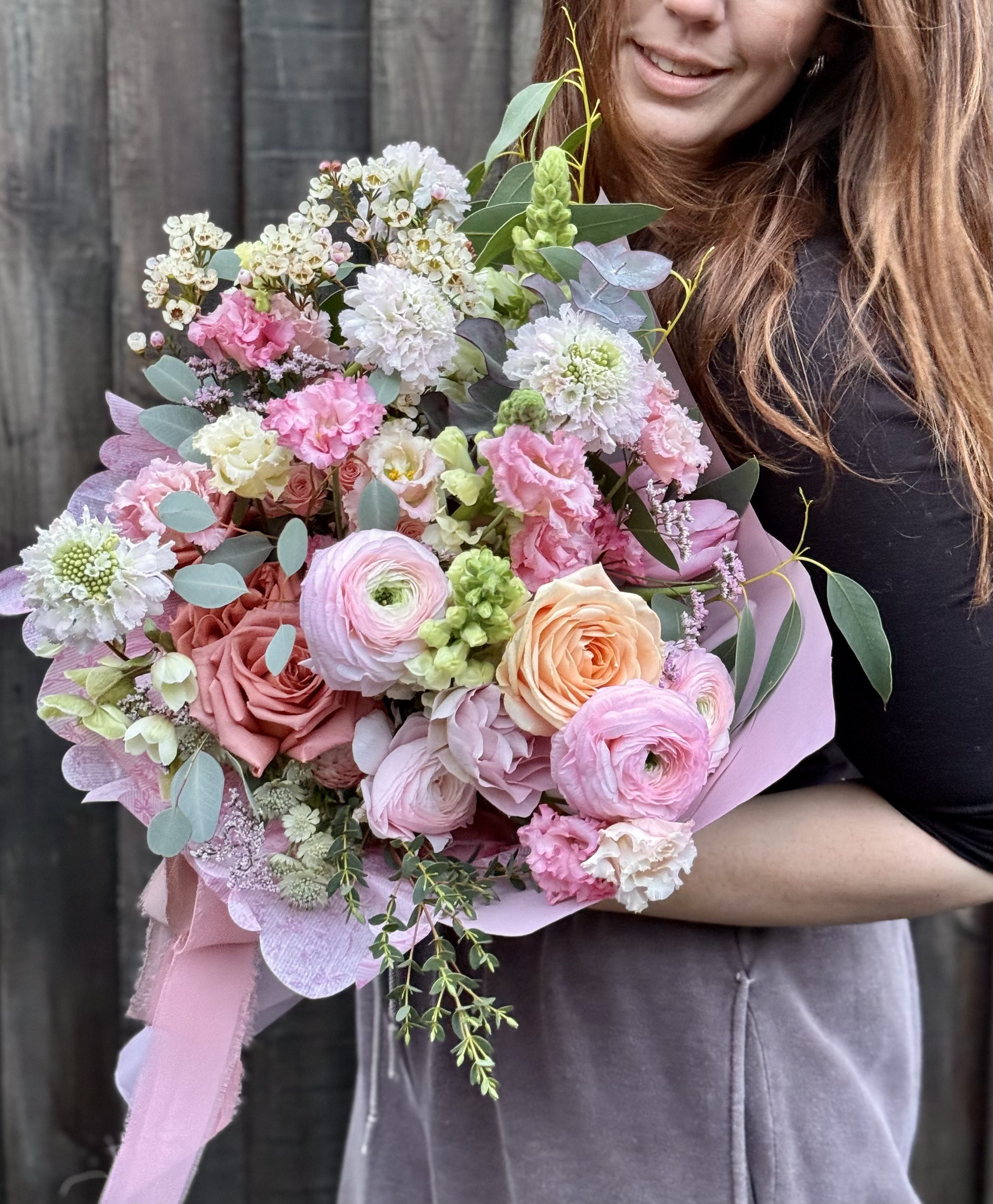 Hayley holding a lush bouquet of pink ranunculus, roses and eucalyptus