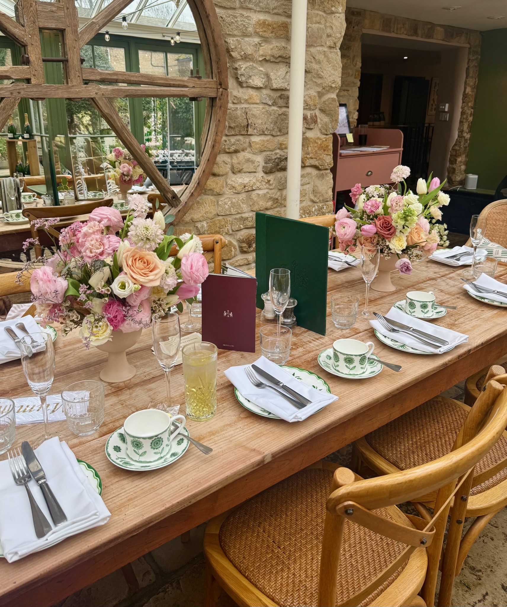 A rustic dining table set with pink floral arrangements at Burrough Court