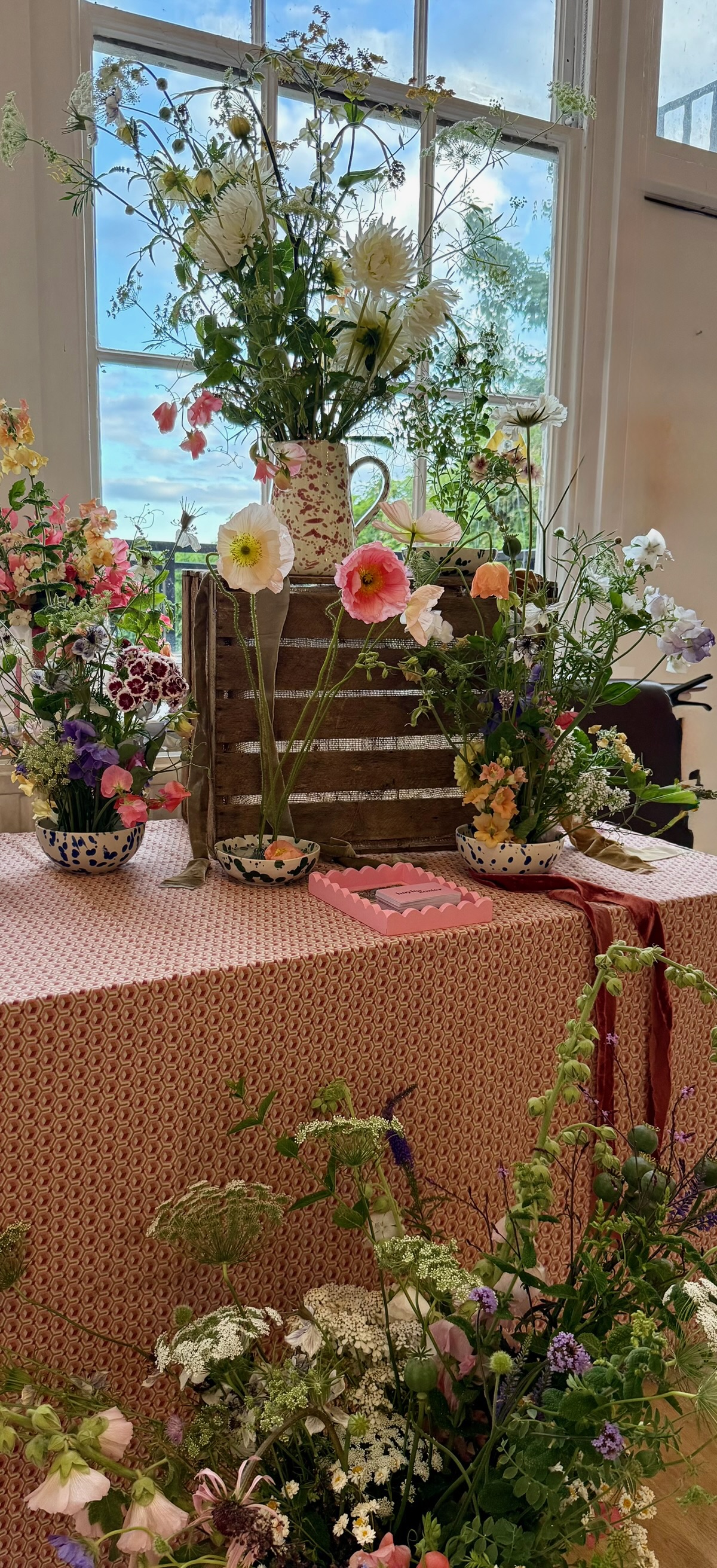 A floral workshop display table with wildflowers, poppies and vintage crates by a window